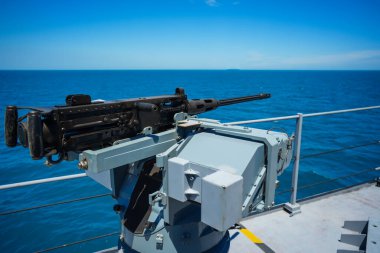 Color image of an automated machine gun on the deck of a military ship, at sea.