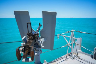 Color image of an automated machine gun on the deck of a military ship, at sea.