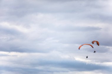 Gri bulutlu gökyüzüne karşı uçan bazı paraşütçülerin görüntüsü.