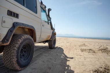 Off road vehicle parked on an empty sandy beach facing the sea.