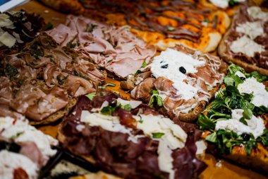 Various flavors pizza cut into square slices on display, in a restaurant.