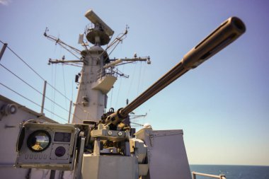 Color image of an automated machine gun on the deck of a military ship, at sea.