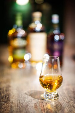 Renk yakın çekim ahşap bir masa üzerinde bir Glencairn viski bardağı, sığ alan derinliği ve arka planda şişe.
