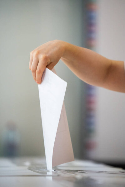 При голосовании на избирательном участке во время выборов лицо вставляет бюллетень в ящик.