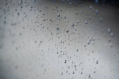 Su damlaları cam bir pencereye düşer, sığ bir alan derinliği vardır..