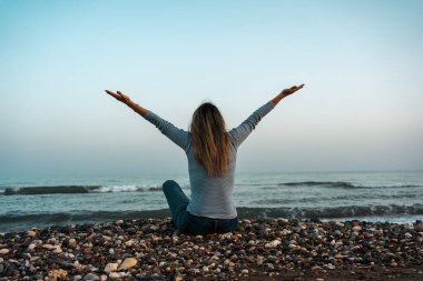 Alacakaranlıkta kumsalda kolları açık oturan bir kadın. Yüksek kalite fotoğraf