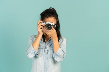 Genç bayan fotoğrafçı beyaz arka planda kamerayla fotoğraf çekiyor.