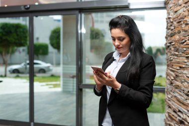 Resmi takım elbiseli gülümseyen iş kadını ofiste akıllı telefon gibi görünüyor. Yüksek kalite fotoğraf