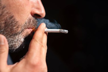 Sakallı adamın çakmak tutup siyah arka planda sigara içtiği yakın plan.