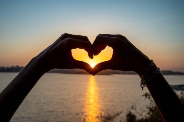 Silhouette of Hands Forming Heart Shape Around Sunset Over the Sea. High quality photo