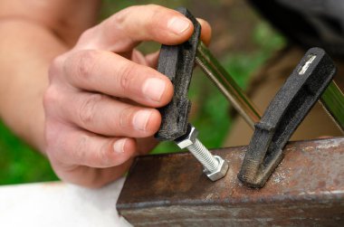 Bir adamın eli bir civatayı metal bir fındığa vidalıyor. Metalle çalışmak