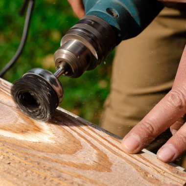 Erkek el fırçalama makinesini tutuyor. Metal disk ile bir tahta parçasını zımparalıyor..