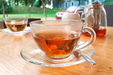 Açık bir kafenin masasında şeffaf bir bardak çay duruyor.