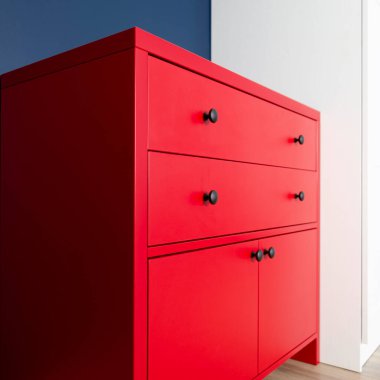 Dairenin iç kısmında, mavi bir duvar ve beyaz bir dolabın arka planında duran kırmızı bir çekmece.