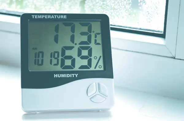 装有温度计的湿度计站在窗台上 带有冷凝 塑料窗户 图库图片