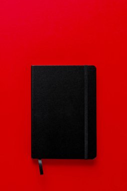 Kırmızı arka planda yer imi olan siyah defter. en üstteki görünüm