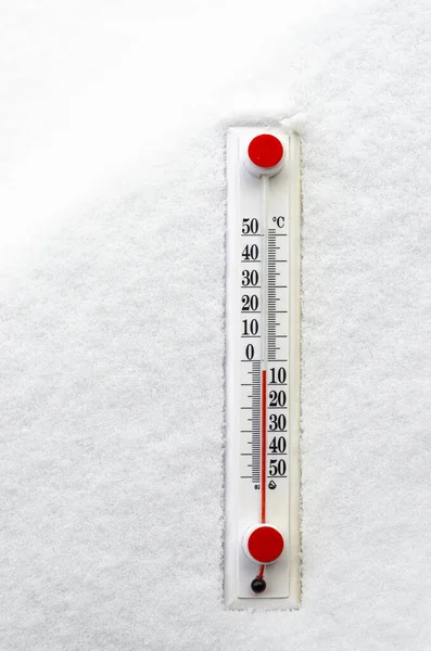 Temperature. A white thermometer with a red scale lies on white snow. Winter.