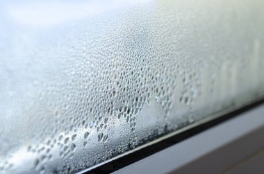 Sera etkisi. Metal-plastik bir pencerenin camındaki buğulanma damlaları.