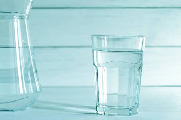 A full glass of clean water and a jug of water on a white background