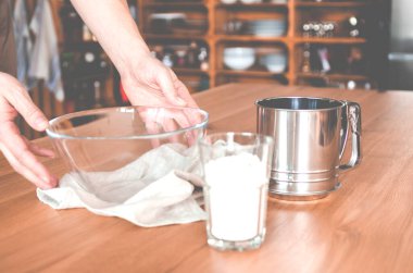 Bir el ahşap bir masanın üzerindeki cam bir kaseye uzanıyor, sofra takımı ve içecek takımı ile çevrili. Tuz ve biberlikler rafın yanında duruyor.