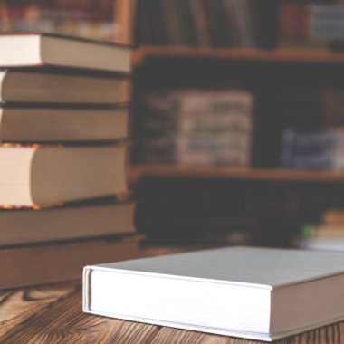 Kitap raflarının arka planına karşı tahta bir masa üzerinde beyaz kitap