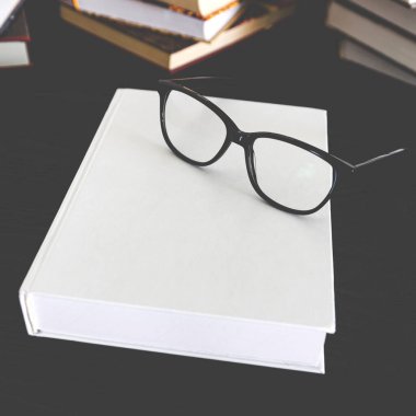 Siyah bir masada siyah okuma gözlüğü ve yazı için yeri olan beyaz kitap.