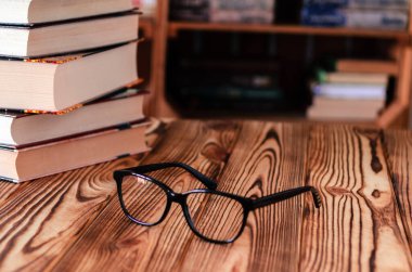 Masaüstünde eski kitapların arka planına karşı okuma gözlüğü. Kitaplıklar
