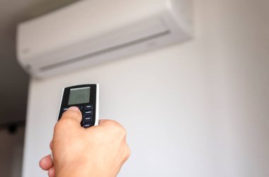 Klimanın uzaktan kumandası klimanın arka planına dayanan bir adamın elinde. İklim denetimi