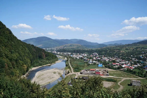 Yazın dağlarda doğal manzara. Parlak mavi gökyüzü ile güneşli kırsal manzara. Doğa koruma kavramı. Nehir ve küçük evlerle dağ köyünün nefes kesici manzarası.