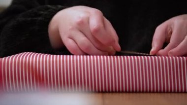 Kırmızı kurdeleyle hediye paketi yapan bir kadın. Eller kırmızı ve beyaz yılbaşı kağıdında bir kutu paketliyor.. 