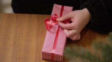 Kırmızı kurdeleyle hediye paketi yapan bir kadın. Eller kırmızı ve beyaz yılbaşı kağıdında bir kutu paketliyor.. 