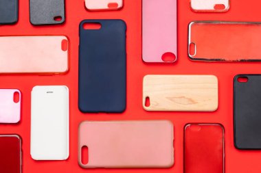 Cep telefonu için çok renkli plastik kapaklar yığını. Kırmızı arka planda akıllı telefon koruyucusu aksesuarları. Bir sürü silikon telefon ve deri yan yana.