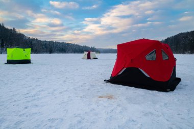 Ice fishing tent on a frozen lake at sunset. Fisherman camp on a peaceful winter evening. clipart