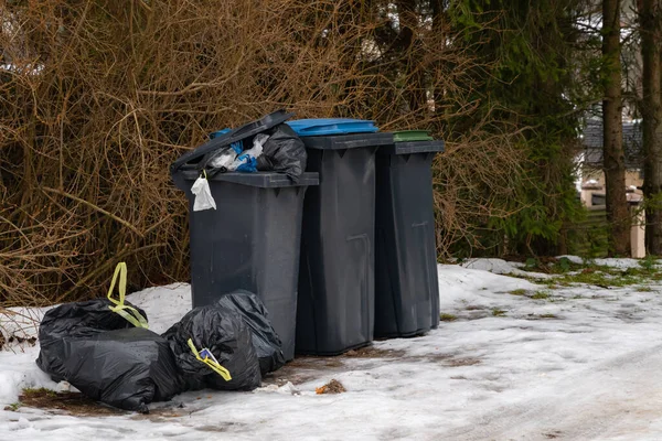 Garbage bin full of trash on white snow in residential area in winter.