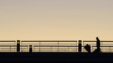 Gün batımında köprüyü geçen bir insanın silueti ve arka planda güzel bir gökyüzü. Adam yaya köprüsünde yürüyor. 