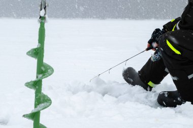 Winter fishing on ice. Man jiggling bait in an ice hole. Relaxing in the wild during snowfall. clipart
