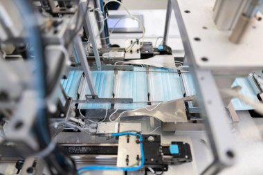 Bir fabrikada yapılan tıbbi yüz maskelerinin yakın çekim süreci. Otomatik makineler büyük miktarlarda solunum maskesi yapıyor..