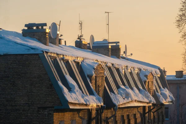 TV and cable antennas on the roof top of an apartment house covered in snow at sunset.