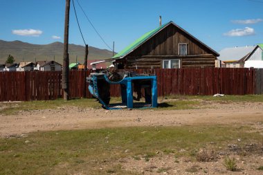 Terk edilmiş arabanın çerçevesi, arka plandaki çit ve ev. Kırsal kesimde otomobil iskeleti duruyor..