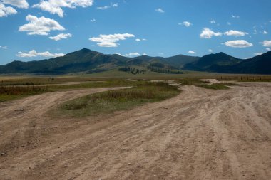 Açık araziler ve arka planda görkemli dağlar. Tepeli kırsal arazi, bulutlu mavi gökyüzü..