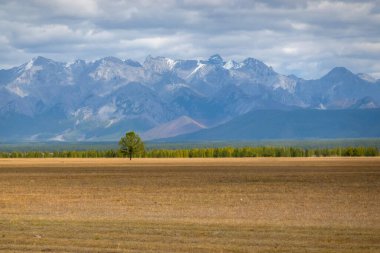 Açık araziler ve arka planda görkemli dağlar. Tepeli kırsal arazi, bulutlu mavi gökyüzü..