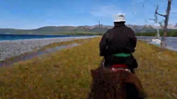 コブスゴル モンゴル 2022年9月 遊牧民の男が湖の岸に馬に乗って 地平線の雲と青空 馬の後ろに野生動物 水と山を歩く — ストック動画