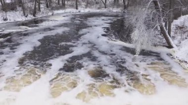 Buzlu ağaç dalları akan baraj suyunun üzerinde. Soğuk bir günde, su akıntısında beyaz köpük 