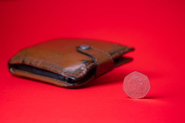 English money - fifty pence on red backdrop. Blurred wallet in the background. Saving money for future.