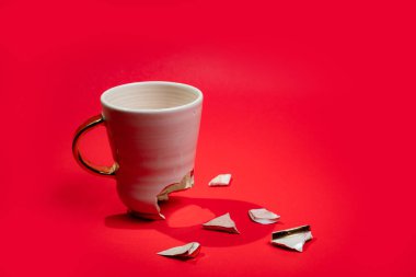 Broken tea cup isolated on red background. Cracked coffee mug and fragile ceramic pieces