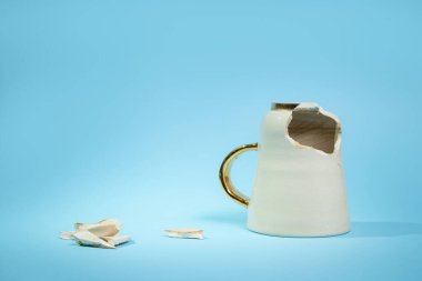 Broken tea cup isolated on blue background. Cracked coffee mug and fragile ceramic pieces