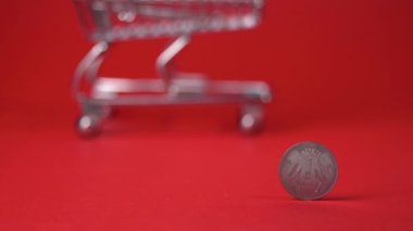 Rupee coin on red backdrop. Blurred empty shopping trolley in the background. Inflation, saving money for shopping. 