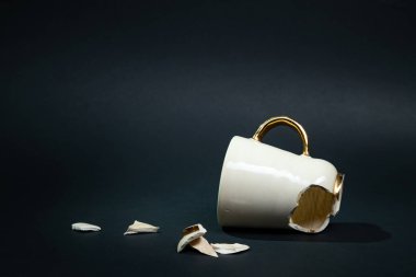 Broken tea cup isolated on black background. Cracked coffee mug and fragile ceramic pieces