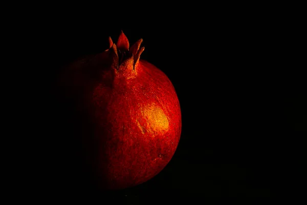 Ripe pomegranate fruit on a black background, close-up. Sweet red fruit.
