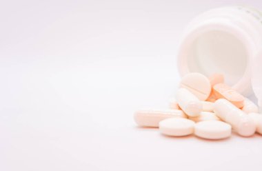 Beyaz bir arka planda, açık beyaz bir kutudan dökülen haplar ve kapsüller gösteriliyor. Farklı şekil ve renklerde ilaçlar: yuvarlak, oval ve kapsüller, çoğunlukla beyaz ve turuncu tonlarda.
